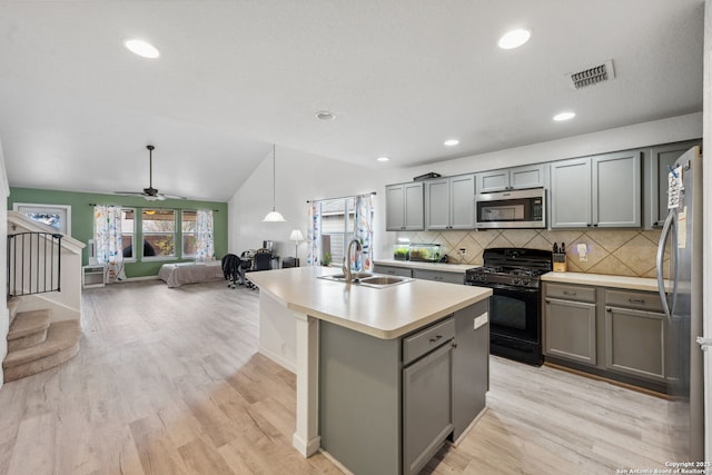 kitchen featuring sink, stainless steel appliances, decorative backsplash, lofted ceiling, and a kitchen island with sink