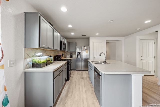 kitchen with sink, backsplash, an island with sink, appliances with stainless steel finishes, and light wood-type flooring