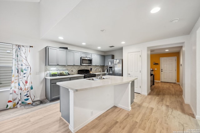 kitchen featuring sink, backsplash, gray cabinets, a center island with sink, and appliances with stainless steel finishes