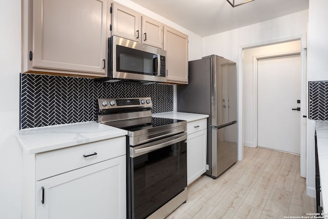 kitchen with white cabinetry, light stone countertops, stainless steel appliances, tasteful backsplash, and light wood-type flooring