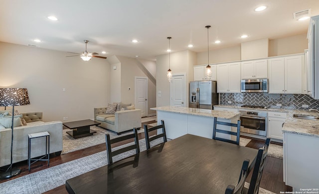 kitchen featuring backsplash, stainless steel appliances, white cabinetry, and hanging light fixtures