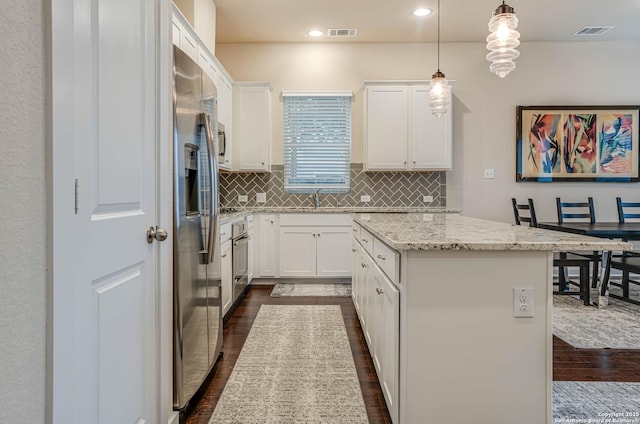 kitchen with white cabinets, appliances with stainless steel finishes, decorative light fixtures, a kitchen island, and light stone counters