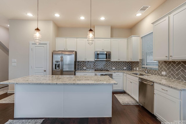 kitchen with pendant lighting, stainless steel appliances, a kitchen island, and white cabinetry