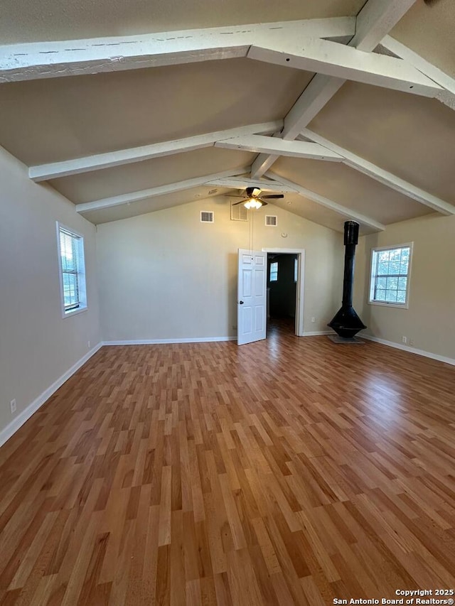 unfurnished living room with wood-type flooring, vaulted ceiling with beams, a wood stove, and ceiling fan