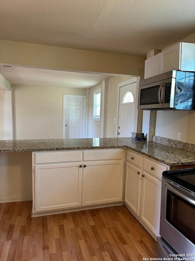 kitchen featuring white cabinets, appliances with stainless steel finishes, a textured ceiling, and light stone counters