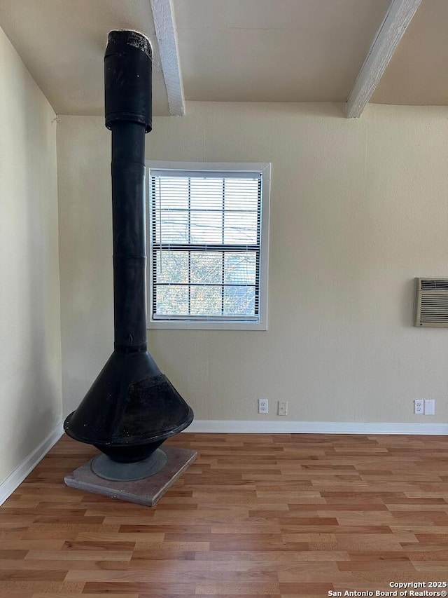 details featuring wood-type flooring, a wood stove, an AC wall unit, and beam ceiling