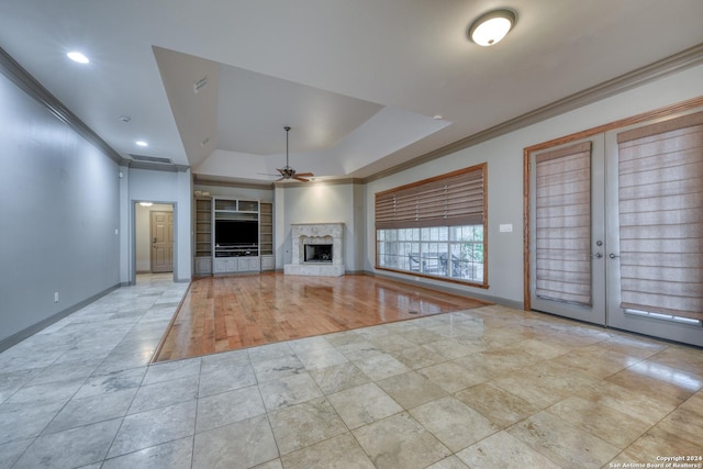 unfurnished living room featuring french doors, ceiling fan, built in features, ornamental molding, and a tray ceiling