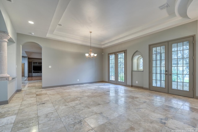 spare room featuring a raised ceiling, french doors, and an inviting chandelier