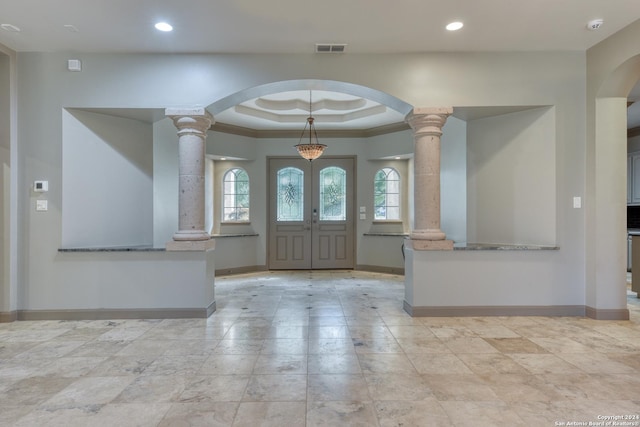 foyer entrance with french doors, a raised ceiling, crown molding, and ornate columns