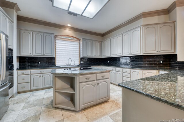 kitchen with dark stone counters, sink, decorative backsplash, ornamental molding, and a kitchen island