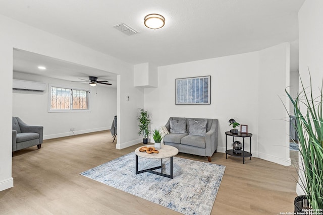 living room featuring a wall mounted air conditioner, ceiling fan, and light hardwood / wood-style floors