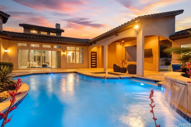 pool at dusk with pool water feature and a patio area