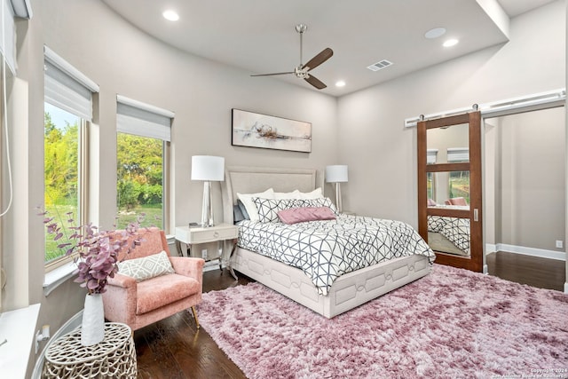 bedroom with a barn door, ceiling fan, and dark wood-type flooring