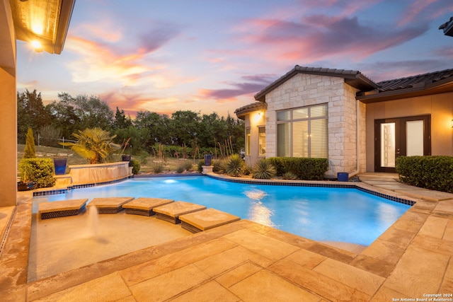 pool at dusk with an in ground hot tub, french doors, and pool water feature