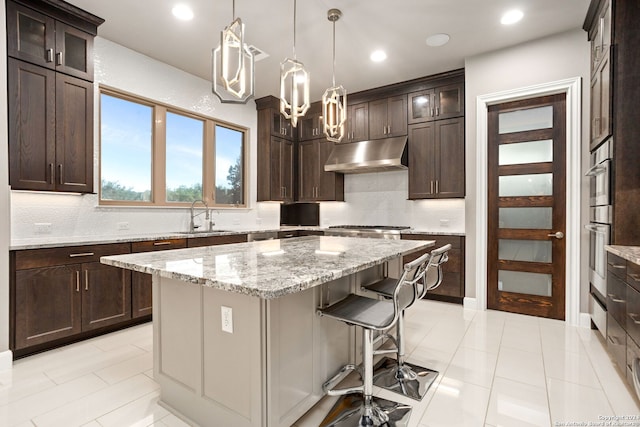 kitchen with light stone countertops, a kitchen breakfast bar, sink, a kitchen island, and hanging light fixtures