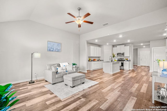 living room featuring ceiling fan, light wood-type flooring, sink, and vaulted ceiling