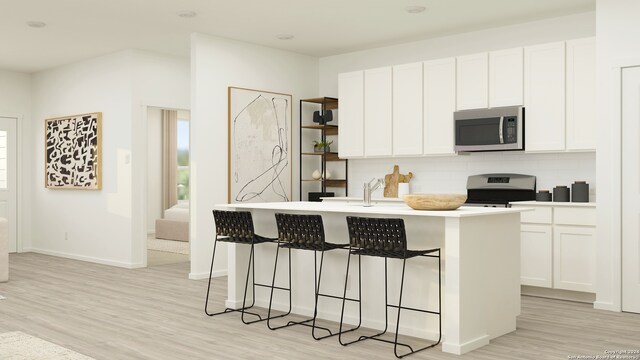 kitchen featuring stove, backsplash, light wood-type flooring, a kitchen island with sink, and white cabinets