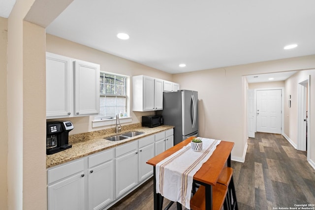 kitchen with stainless steel fridge, light stone counters, sink, white cabinets, and dark hardwood / wood-style floors