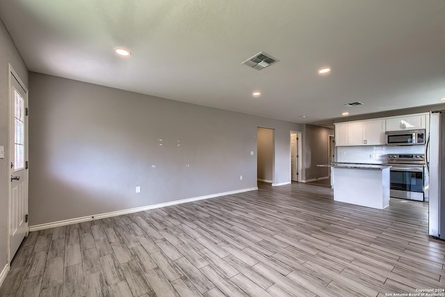 kitchen featuring stainless steel appliances, white cabinets, backsplash, light hardwood / wood-style floors, and a kitchen island