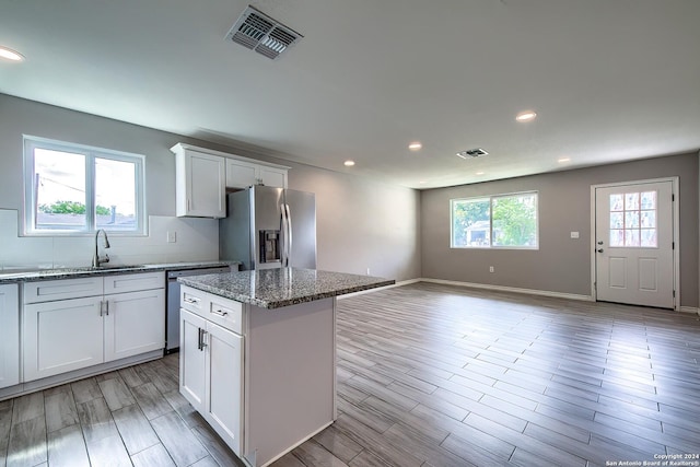 kitchen featuring a center island, sink, appliances with stainless steel finishes, light stone counters, and white cabinetry