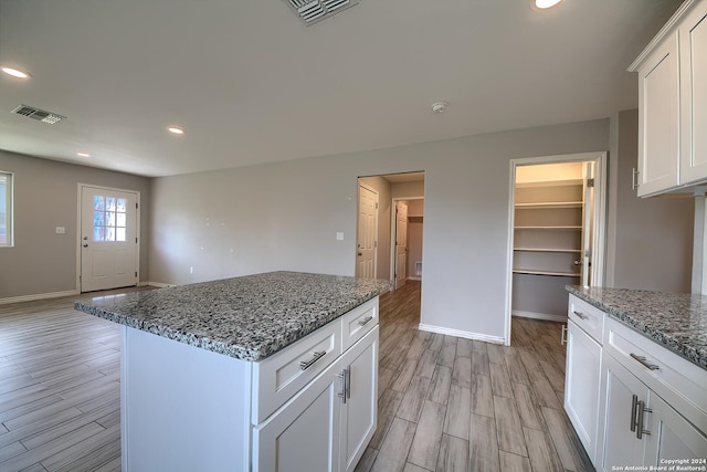 kitchen featuring stone counters, a center island, white cabinets, and light wood-type flooring