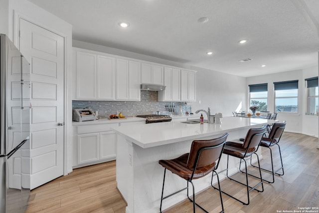 kitchen featuring sink, an island with sink, a kitchen bar, white cabinets, and range