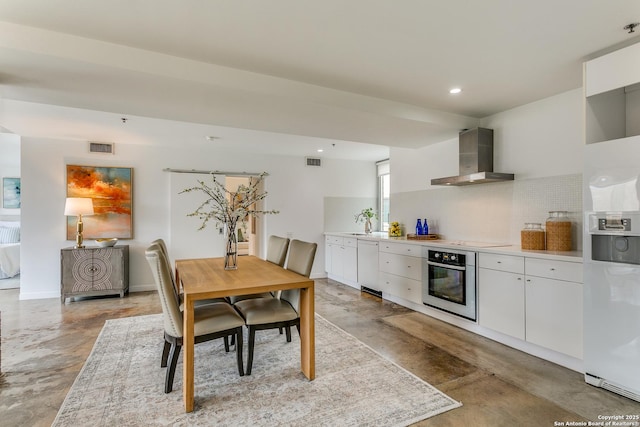 kitchen with wall chimney range hood, decorative backsplash, white cabinets, and white appliances