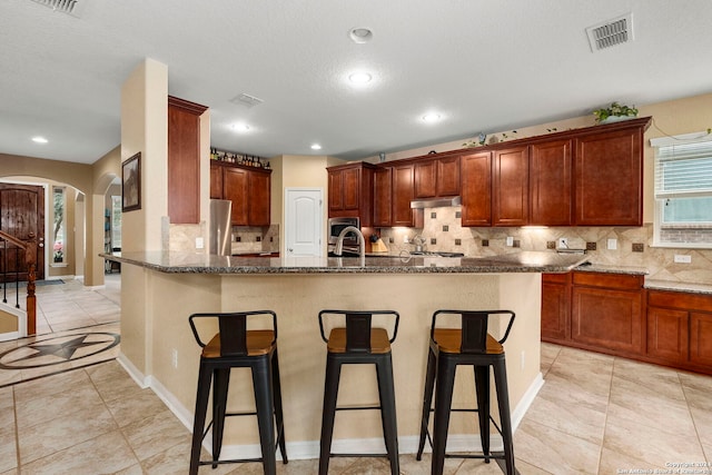 kitchen with sink, dark stone counters, a kitchen bar, light tile patterned flooring, and appliances with stainless steel finishes