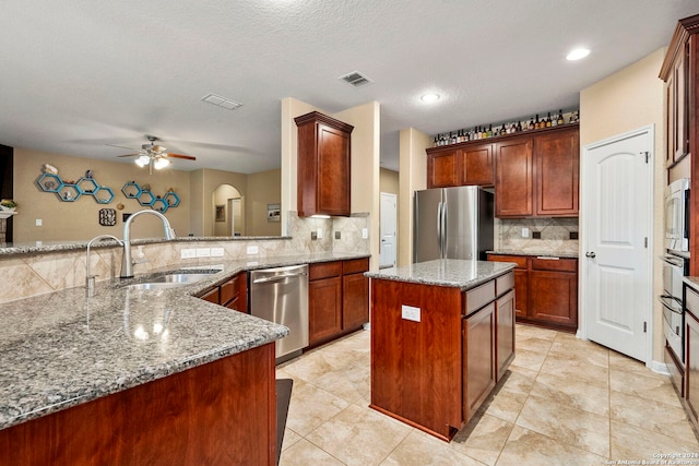 kitchen featuring a center island, sink, ceiling fan, light stone countertops, and stainless steel appliances