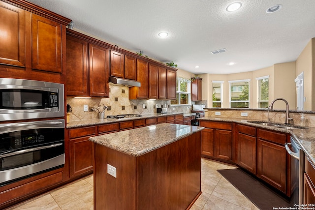 kitchen featuring light stone countertops, backsplash, stainless steel appliances, and sink