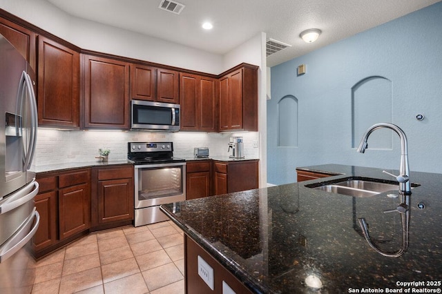 kitchen featuring sink, dark stone countertops, light tile patterned floors, decorative backsplash, and appliances with stainless steel finishes