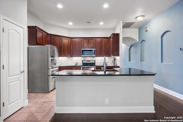 kitchen with appliances with stainless steel finishes, an island with sink, light tile patterned flooring, sink, and backsplash