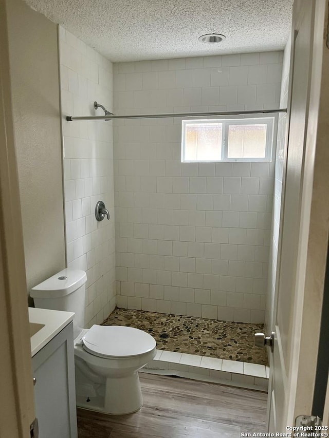 bathroom featuring wood-type flooring, vanity, tiled shower, toilet, and a textured ceiling