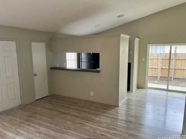 unfurnished living room featuring a textured ceiling, vaulted ceiling, and wood-type flooring