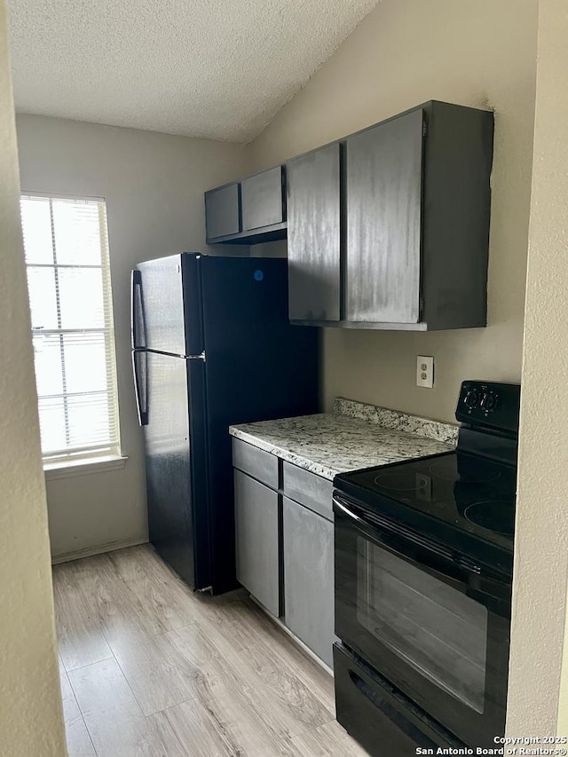 kitchen with lofted ceiling, gray cabinetry, black appliances, light hardwood / wood-style floors, and a textured ceiling