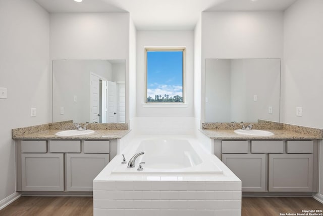 bathroom featuring vanity, wood-type flooring, and a relaxing tiled tub