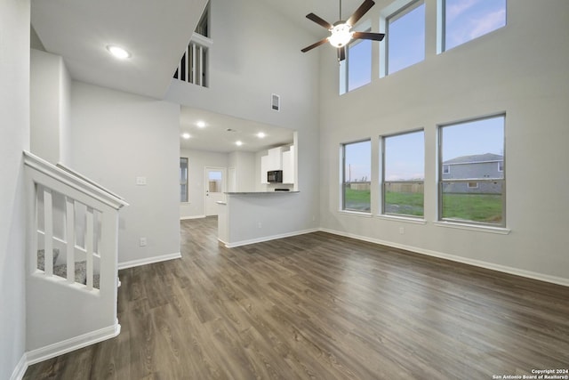 unfurnished living room featuring ceiling fan, a towering ceiling, and dark hardwood / wood-style floors