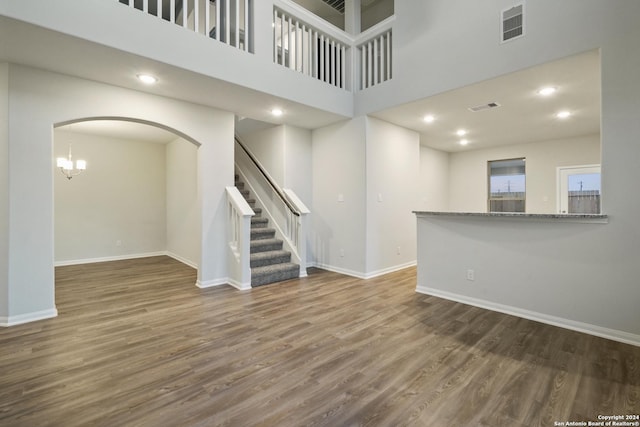 unfurnished living room featuring a chandelier, a towering ceiling, and dark hardwood / wood-style floors