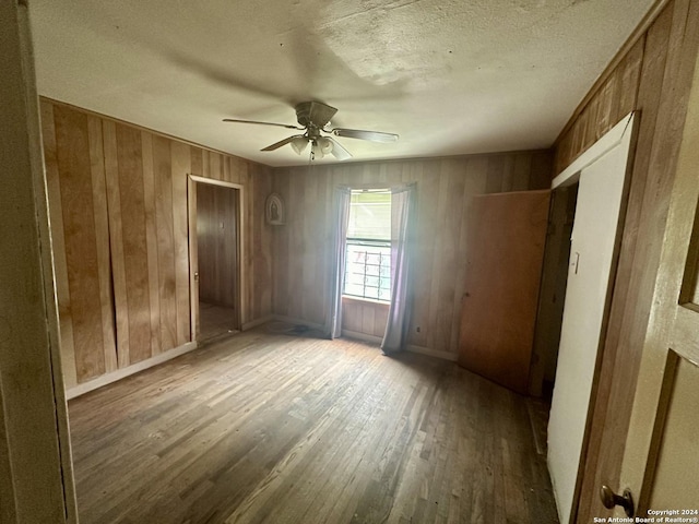 spare room with a textured ceiling, hardwood / wood-style flooring, ceiling fan, and wood walls