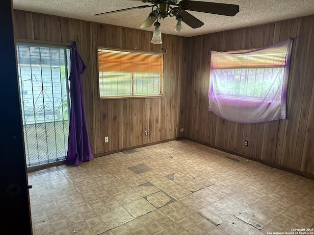 unfurnished room with wood walls, ceiling fan, and a textured ceiling