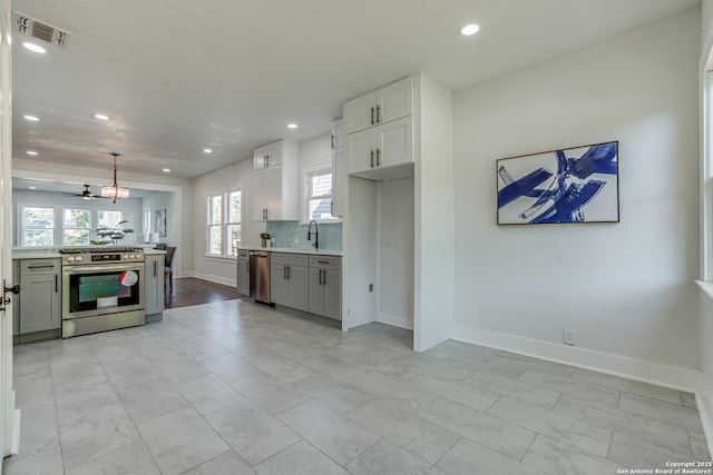 kitchen with appliances with stainless steel finishes, backsplash, sink, white cabinetry, and hanging light fixtures