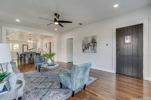 living room with ceiling fan with notable chandelier and dark wood-type flooring