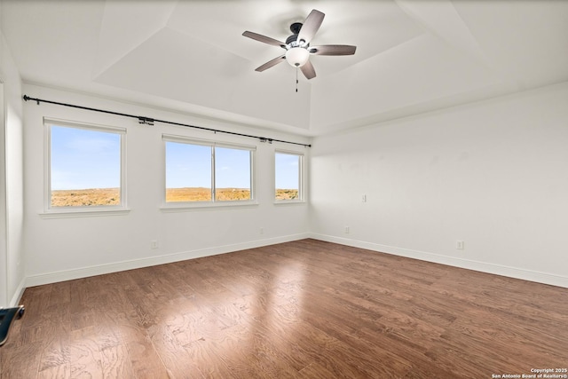 unfurnished room featuring dark hardwood / wood-style floors, ceiling fan, and a tray ceiling