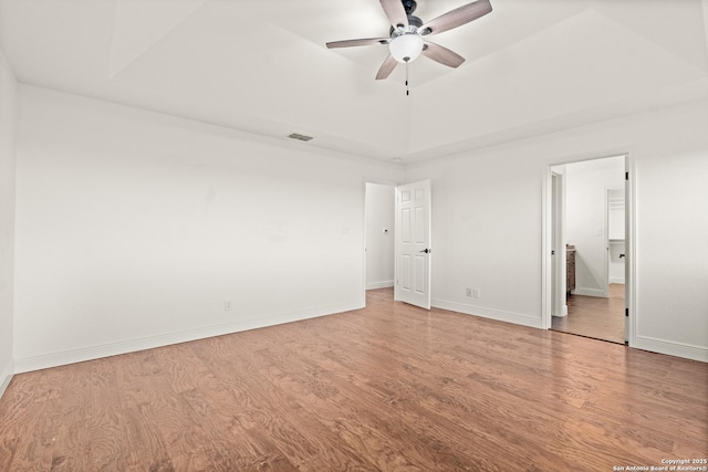 unfurnished bedroom featuring light hardwood / wood-style floors, ensuite bath, ceiling fan, and a tray ceiling