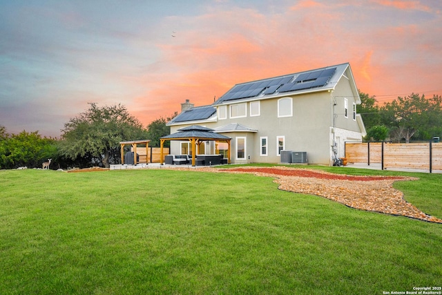 back house at dusk with a gazebo, solar panels, outdoor lounge area, and a lawn