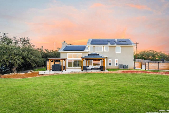 back house at dusk with an outdoor living space, solar panels, a gazebo, a yard, and a patio area