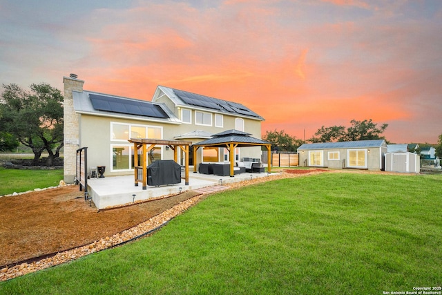 back house at dusk with solar panels, an outdoor hangout area, a shed, a gazebo, and a patio