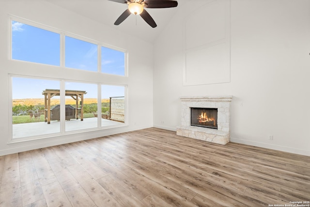 unfurnished living room featuring ceiling fan, a fireplace, high vaulted ceiling, and light wood-type flooring