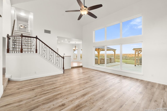 unfurnished living room with ceiling fan with notable chandelier, a towering ceiling, and light hardwood / wood-style floors