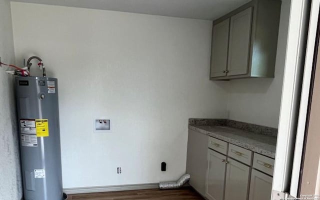 clothes washing area with dark wood-type flooring, cabinets, and electric water heater